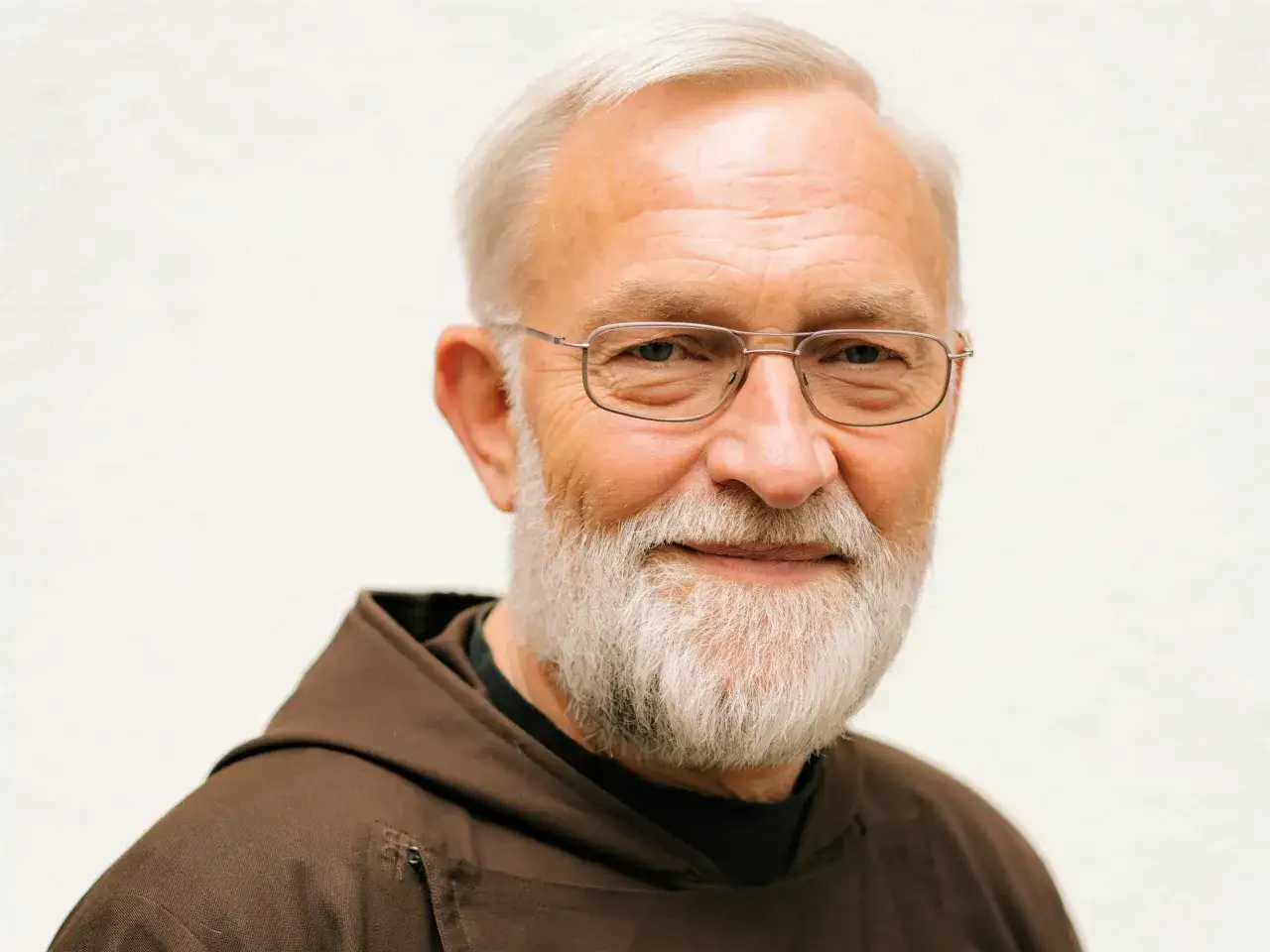 Ein &auml;lterer Mann mit grauem Bart und Haaren, der eine braune M&ouml;nchsrobe tr&auml;gt. Bruder Paulus l&auml;chelt freundlich in die Kamera.