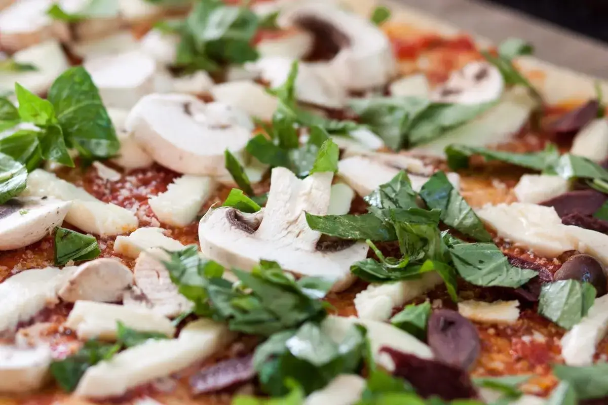 Pizza con champiñones, queso y abundante albahaca italiana fresca.