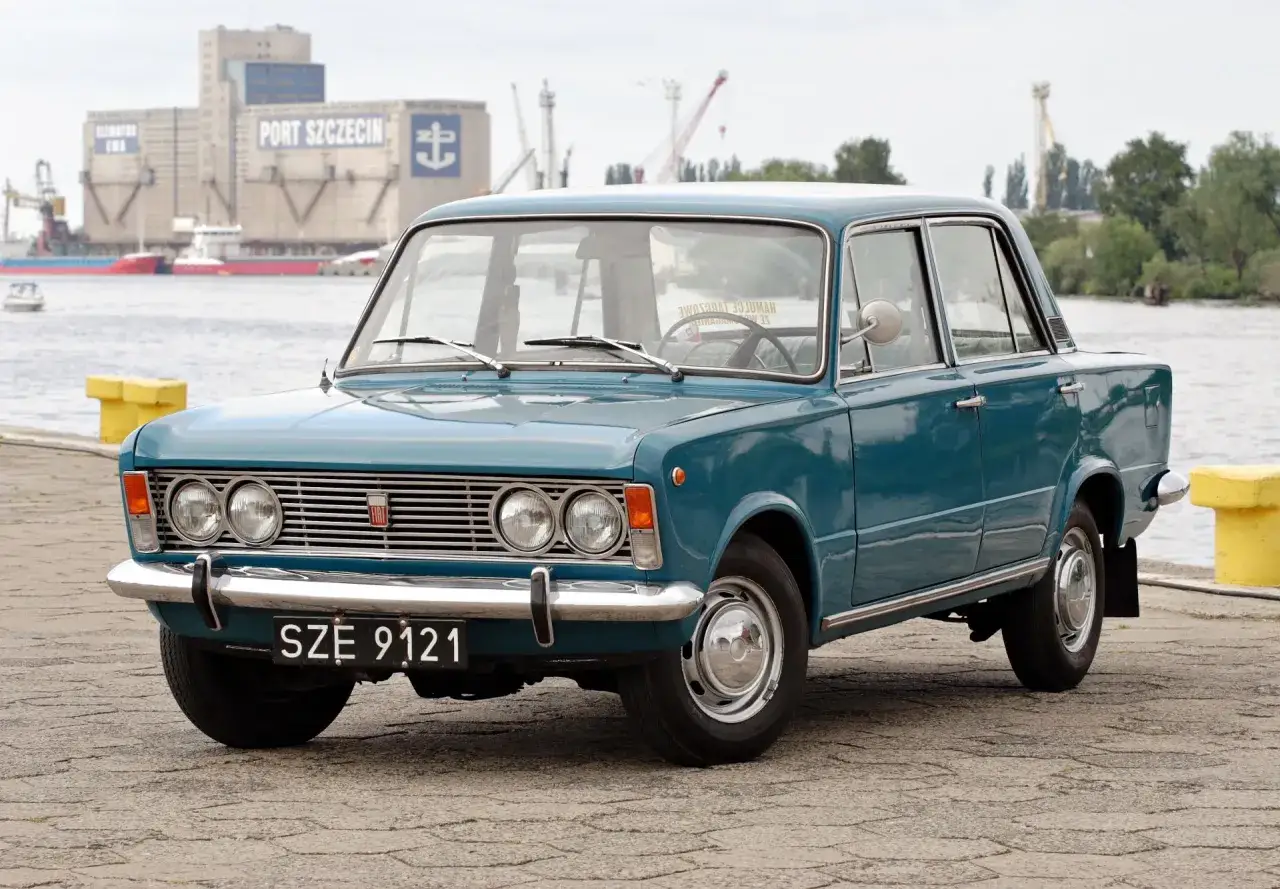 Turkusowy Fiat 125p z czarnymi tablicami rejestracyjnymi SZE 9121 stoi nad wodą, w tle port Szczecin.