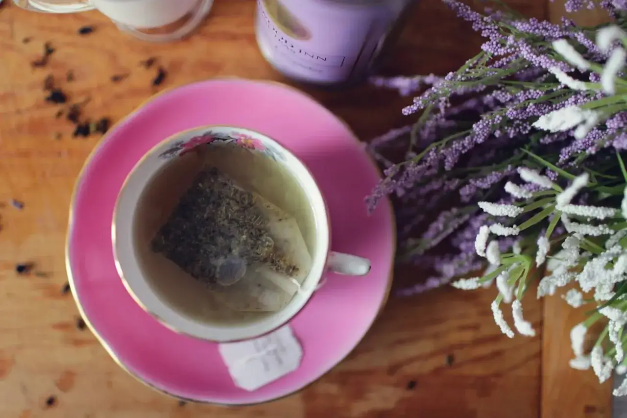 Herbata z lawendy przeciwwskazania. Filiżanka z naparem na r&oacute;żowym spodeczku, obok bukiet lawendy i świeca.