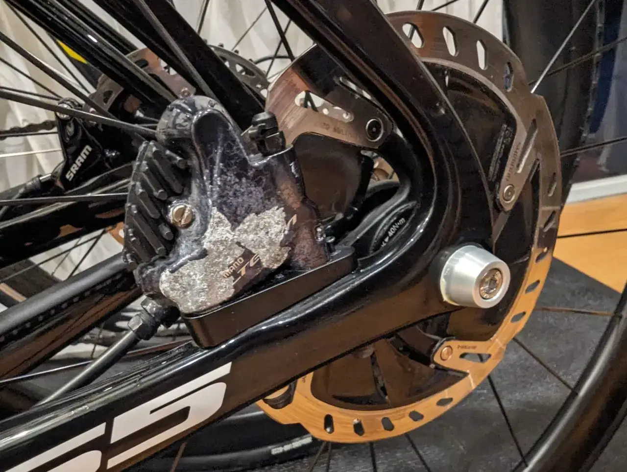 Corroded Shimano brake caliper on a bicycle wheel. This damage shows why is brake fluid corrosive when it leaks onto metal parts.