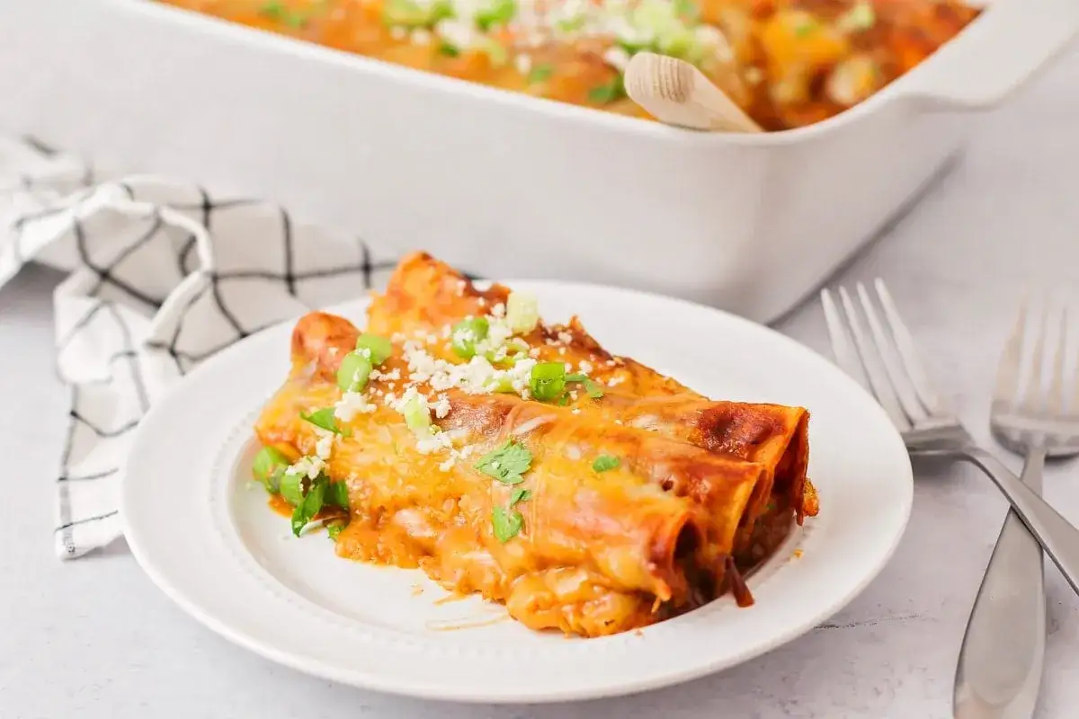 Leckeres Enchiladas Rezept: Gerollte Tortillas mit K&auml;se und So&szlig;e, garniert mit Fr&uuml;hlingszwiebeln und Koriander.