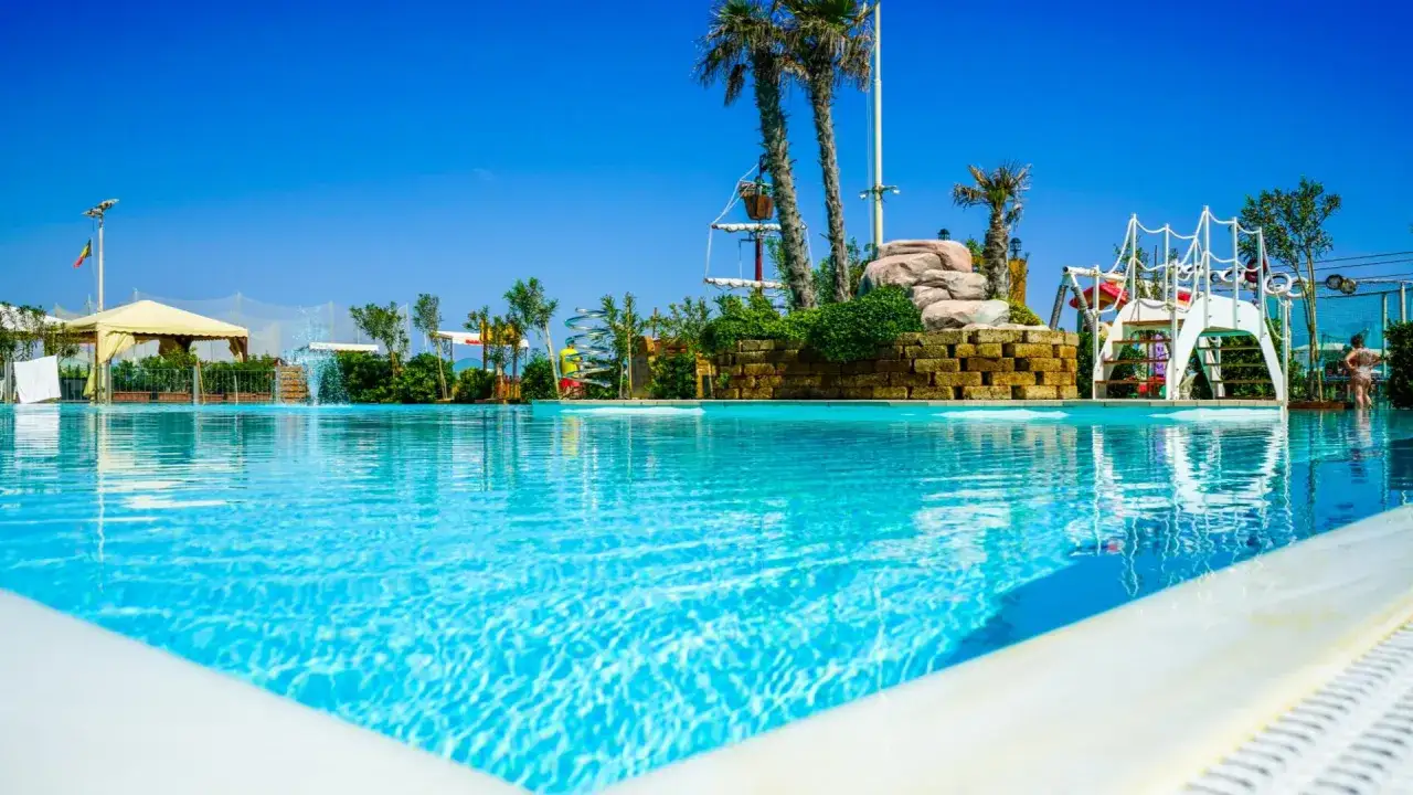 Piscina azzurra e giochi acquatici in un resort a banana beach Gabicce, con palme e cielo limpido.