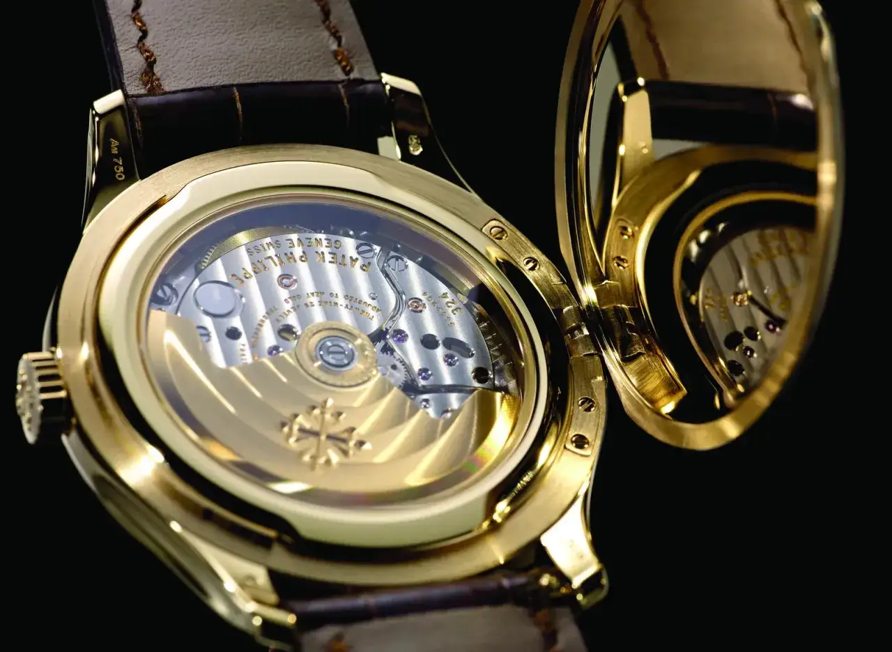 Dettaglio di un orologio Patek Philippe in oro, con il fondello aperto che rivela il calibro di manifattura e la sua finitura impeccabile.