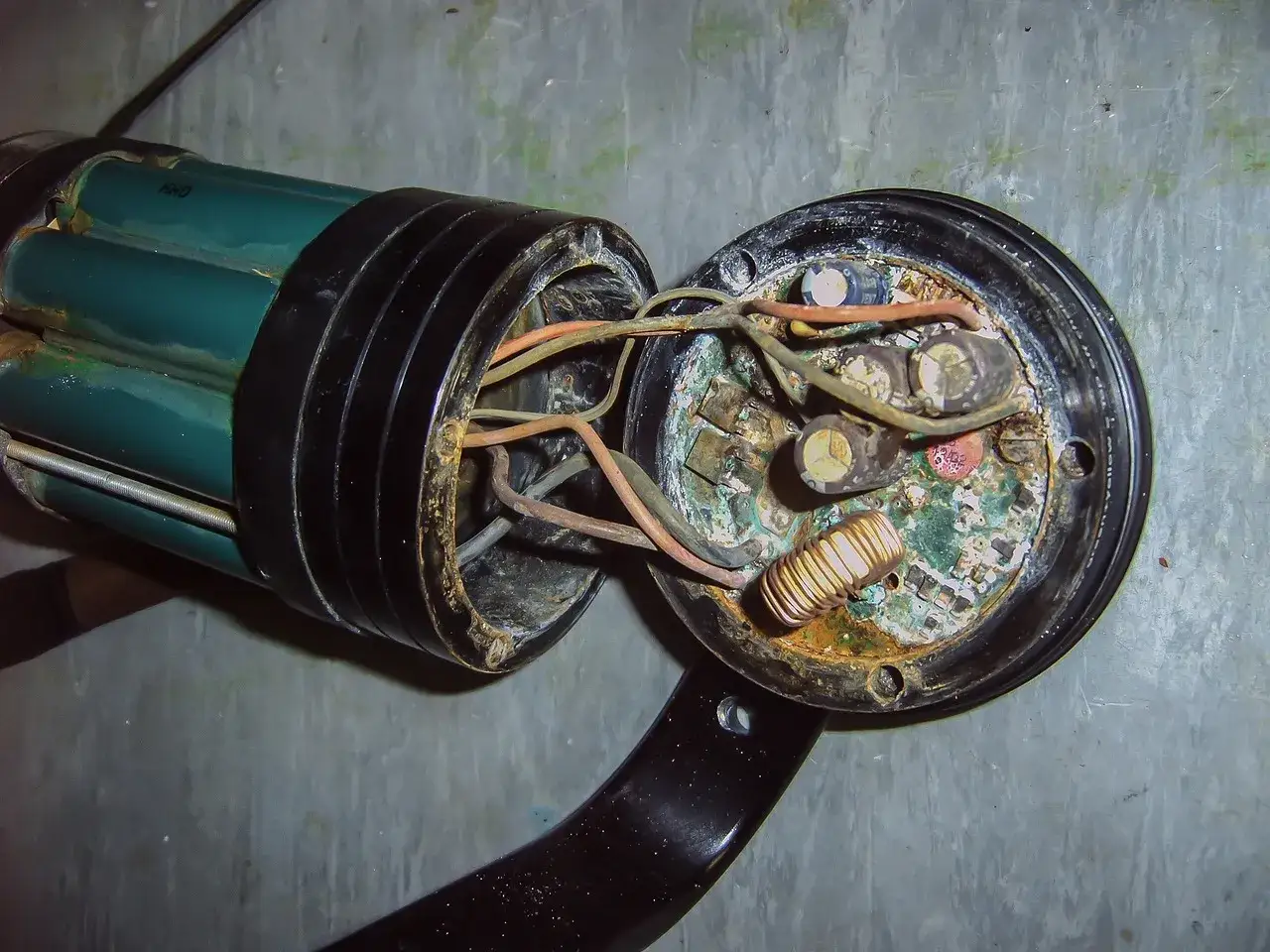 Uszkodzona elektronika z widocznym **zwarcie** na płytce drukowanej, skorodowane elementy i luźne przewody.