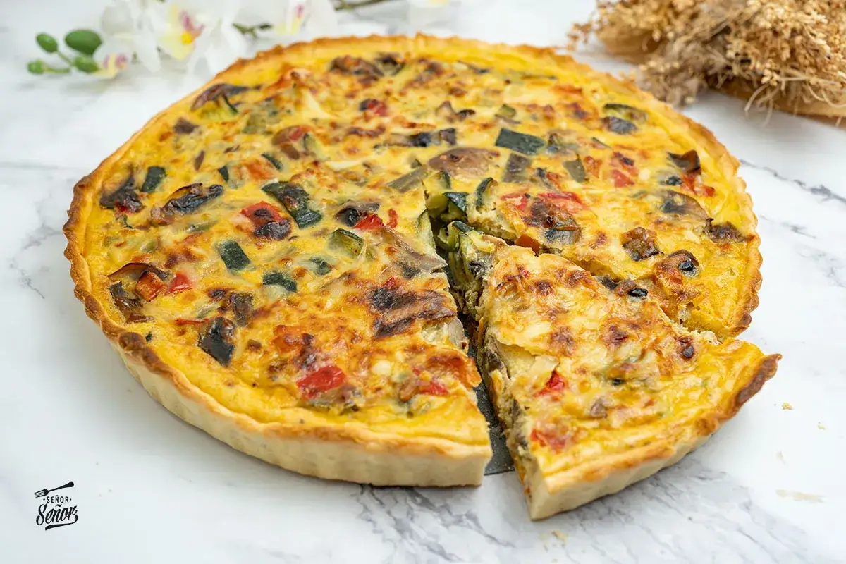 Delicioso quiche vegetal con trozos de calabacín, pimiento y champiñones, horneado hasta dorar.