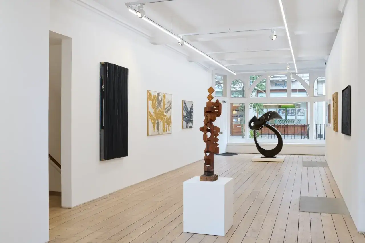 A modern art gallery showcasing diverse types of art galleries, featuring abstract paintings, wooden sculptures, and a sleek black metal piece.