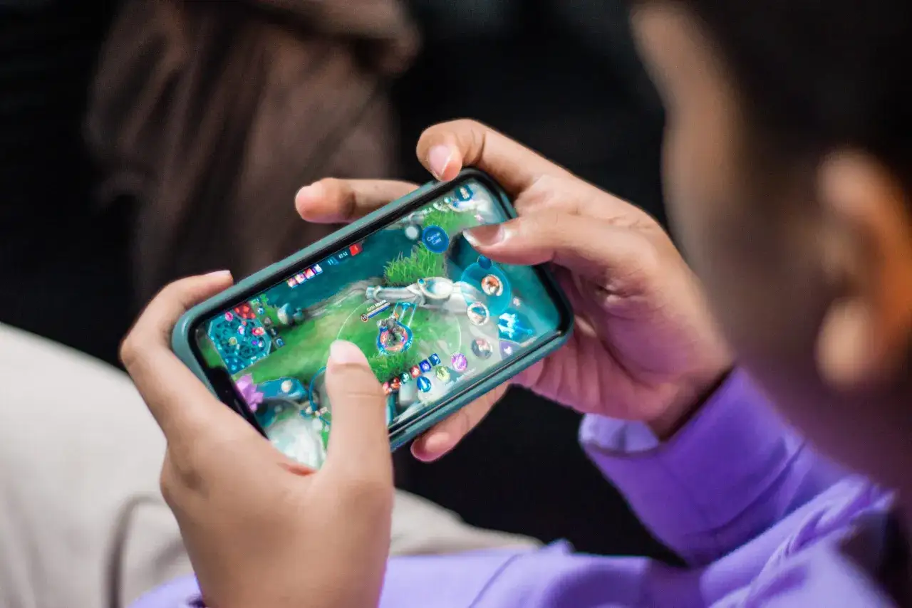 Un jeune joueur concentr&eacute; sur son smartphone, naviguant dans un univers de jeu. Il est en train de d&eacute;couvrir l'un des meilleurs jeux mobile gratuit.