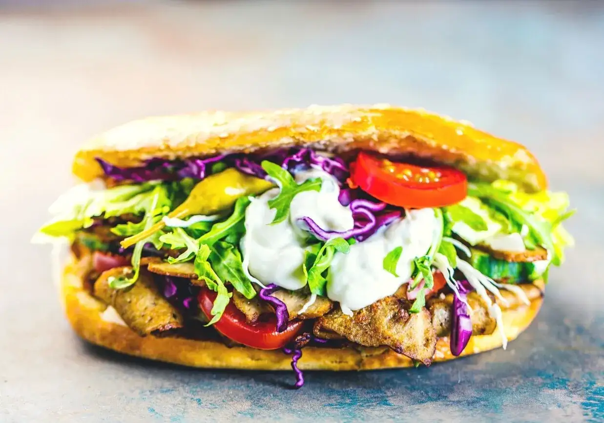Pyszny kebab z indyka w bułce, pełen warzyw: sałaty, pomidorów, czerwonej kapusty i sosu.