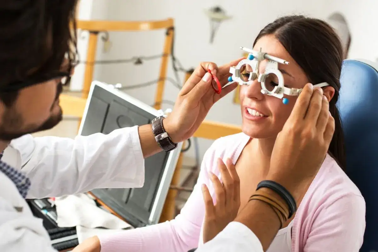 Optometrysta w białym kitlu bada wzrok pacjentki, która ma na nosie oprawkę próbnych soczewek.