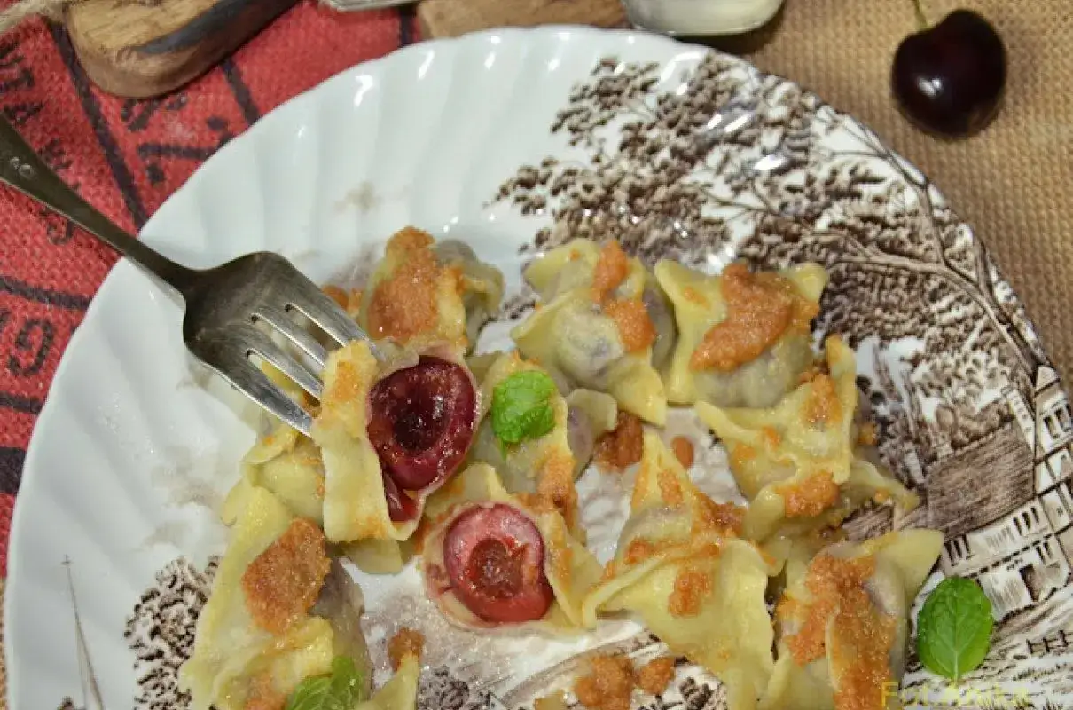 Pyszne pierogi z czereśniami, polane okrasą, na talerzu z motywem drzew. Widok zachęca do spróbowania!