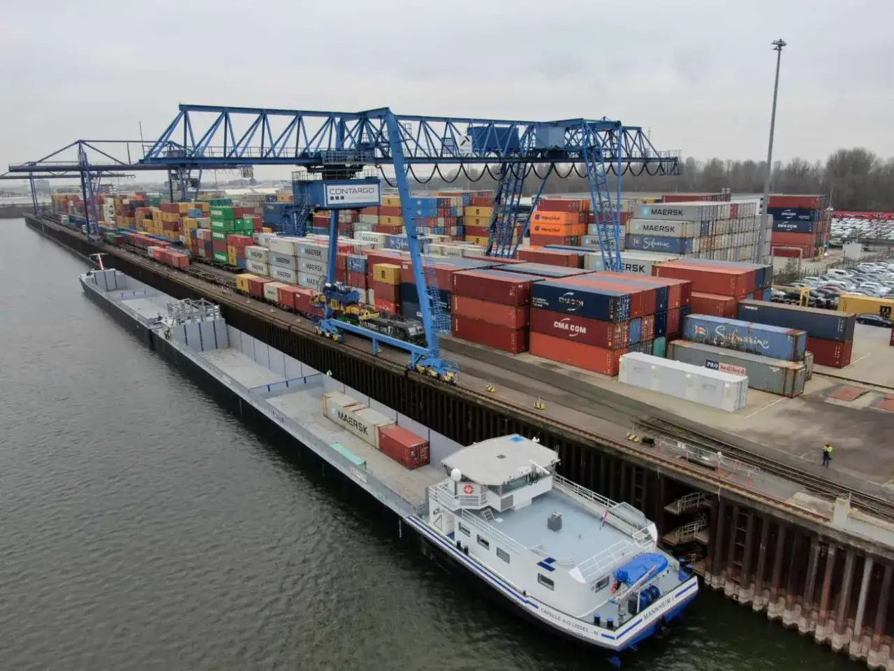 Ein Portagent überwacht das Be- und Entladen von Containern auf ein Schiff und Züge in einem geschäftigen Containerhafen.