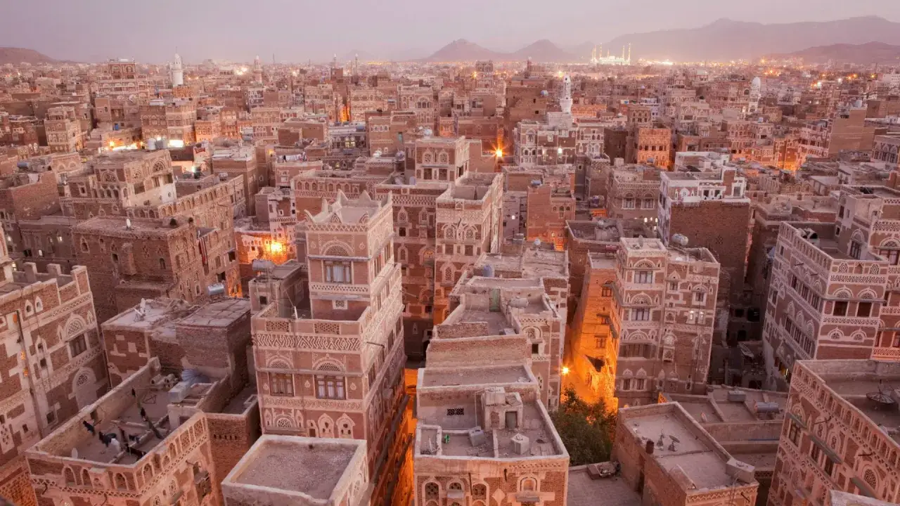 Blick &uuml;ber eine **islamische orientalische Stadt** mit traditionellen Lehmh&auml;usern und Minaretten im Abendlicht.