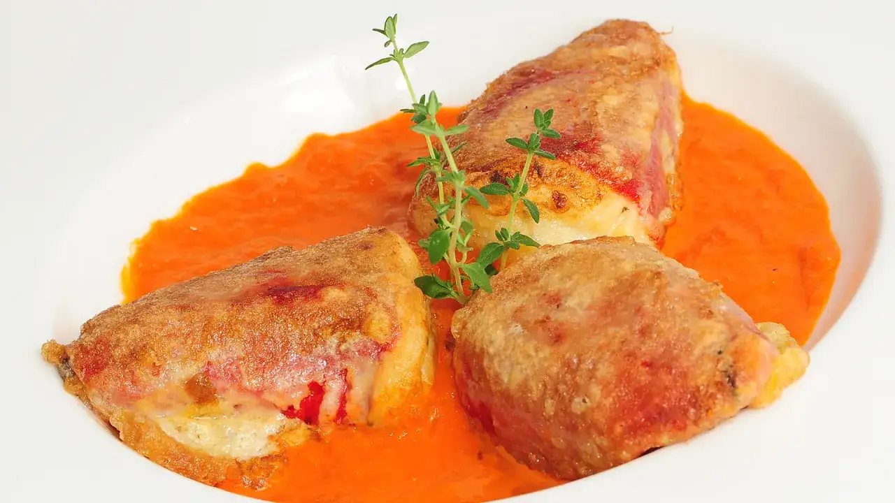 Pimientos rellenos de bacalao, dorados y crujientes, servidos en una cremosa salsa de pimientos rojos, adornados con una ramita de tomillo.