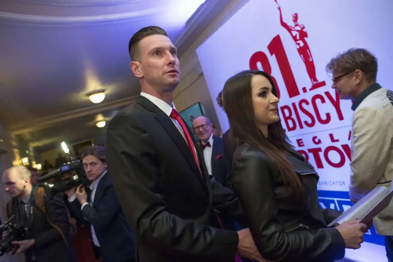 Barbara Gołąb Kadziewicz w czarnej ramonesce obok mężczyzny w garniturze, na tle baneru z napisem