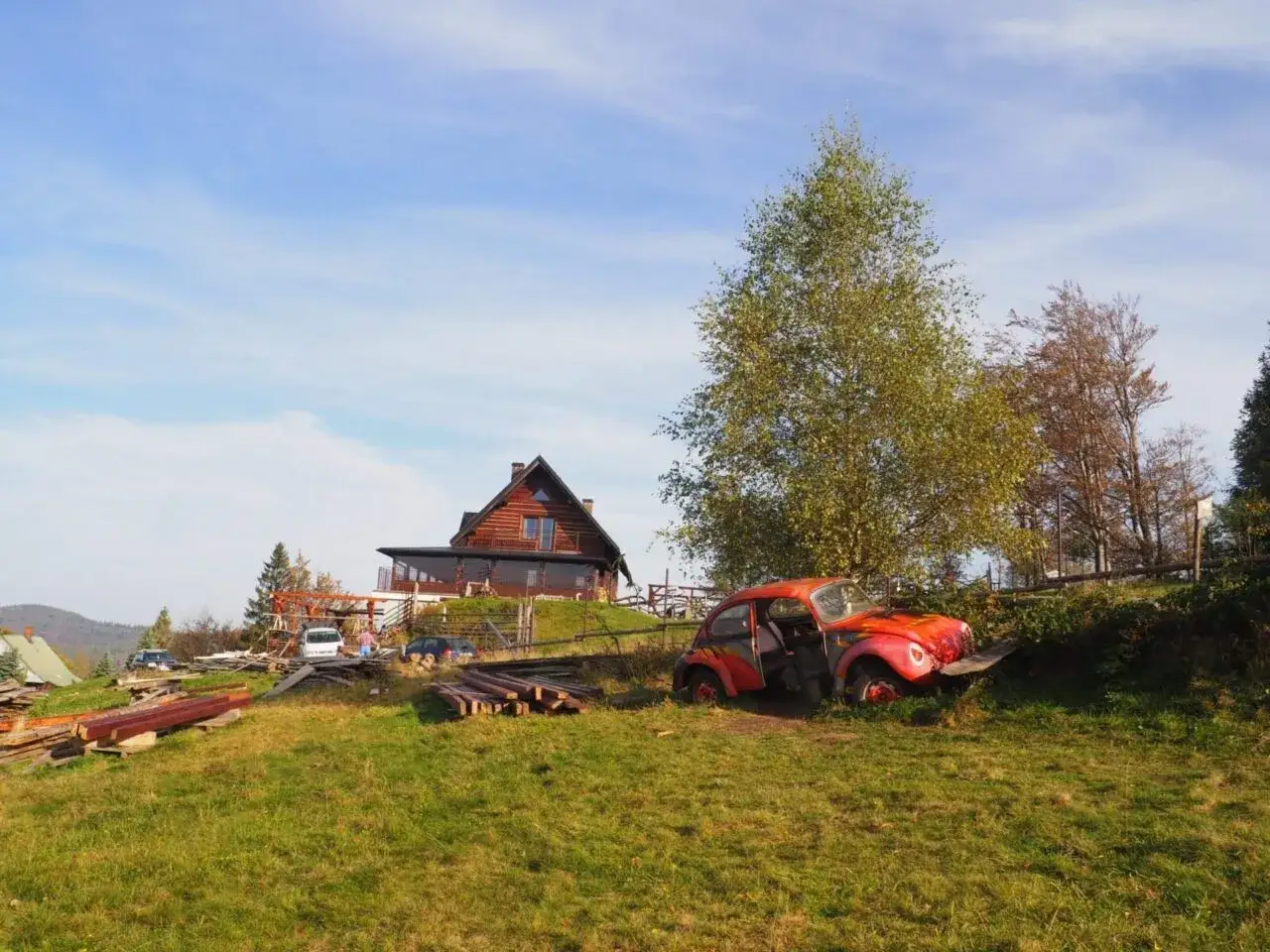 Czerwony garbus na trawie, obok drewniany dom i materiały budowlane. To może być początek szlaku na Trzy Kopce Wiślańskie.
