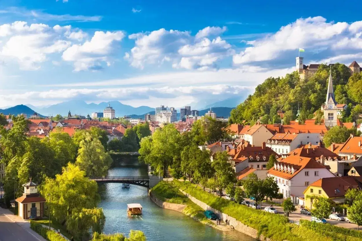 Ljubljana, Sloveniens huvudstad, med floden Ljubljanica, slottet och grönskande kullar under en blå himmel med moln.