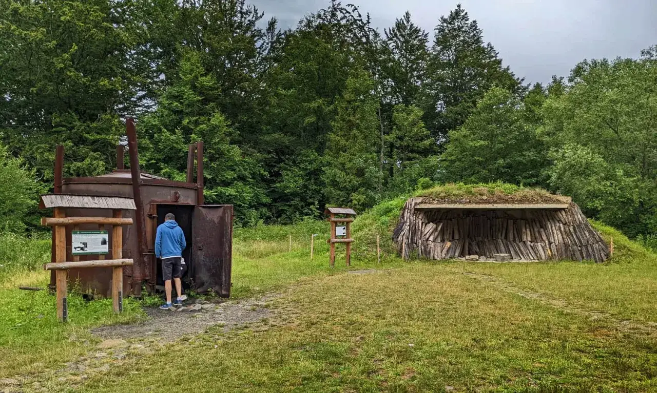 W muzeum wypału węgla drzewnego zwiedzający ogląda piec. Obok znajduje się kopiec z drewnem.
