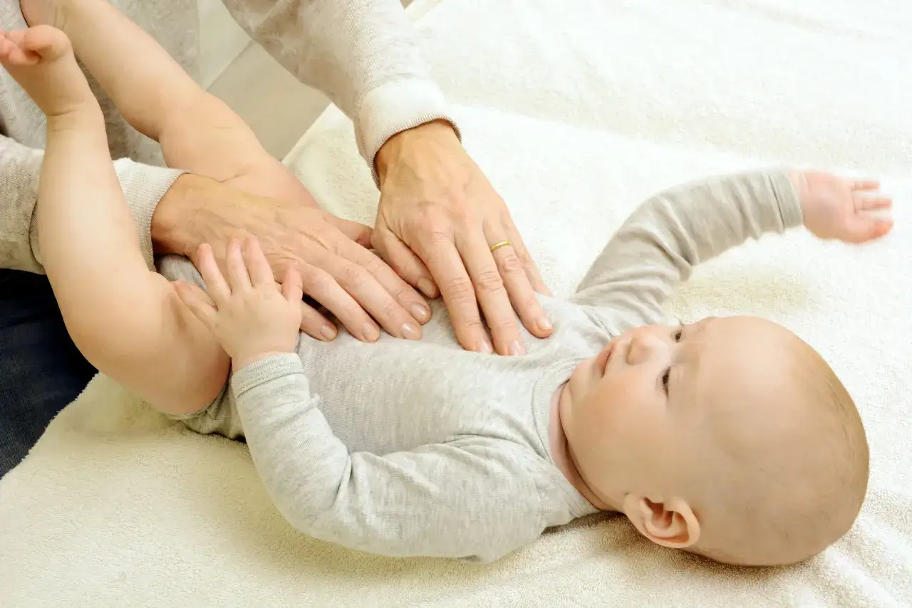 Sanfte H&auml;nde einer Osteopathin behandeln den Bauch eines Babys. Sanfte Ber&uuml;hrungen zur Unterst&uuml;tzung der Entwicklung von Neugeborenen.