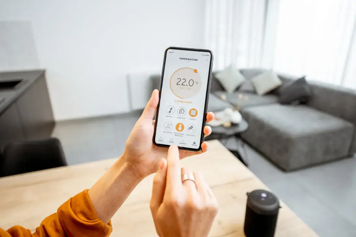Mano ajustando la temperatura en la app de hogar inteligente. Decide cuándo poner la calefacción para estar a 22°C en el salón.