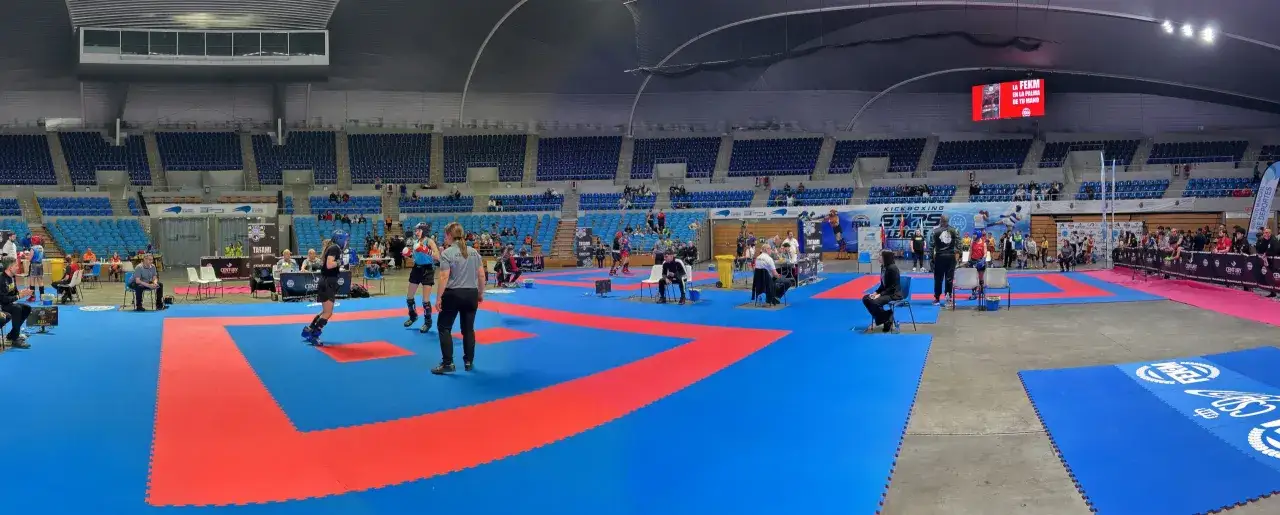 Competici&oacute;n de kickboxing en el Palacio de Deportes Santander. Varios tatamis azules y rojos, competidores con protecciones y p&uacute;blico en las gradas.