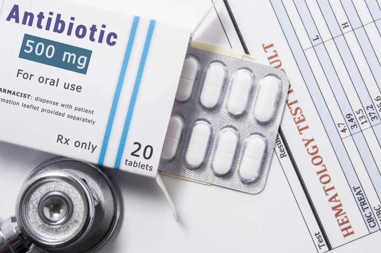 Opakowanie antybiotyku meropenem 500 mg, blister z tabletkami, stetoskop i wyniki badań hematologicznych.