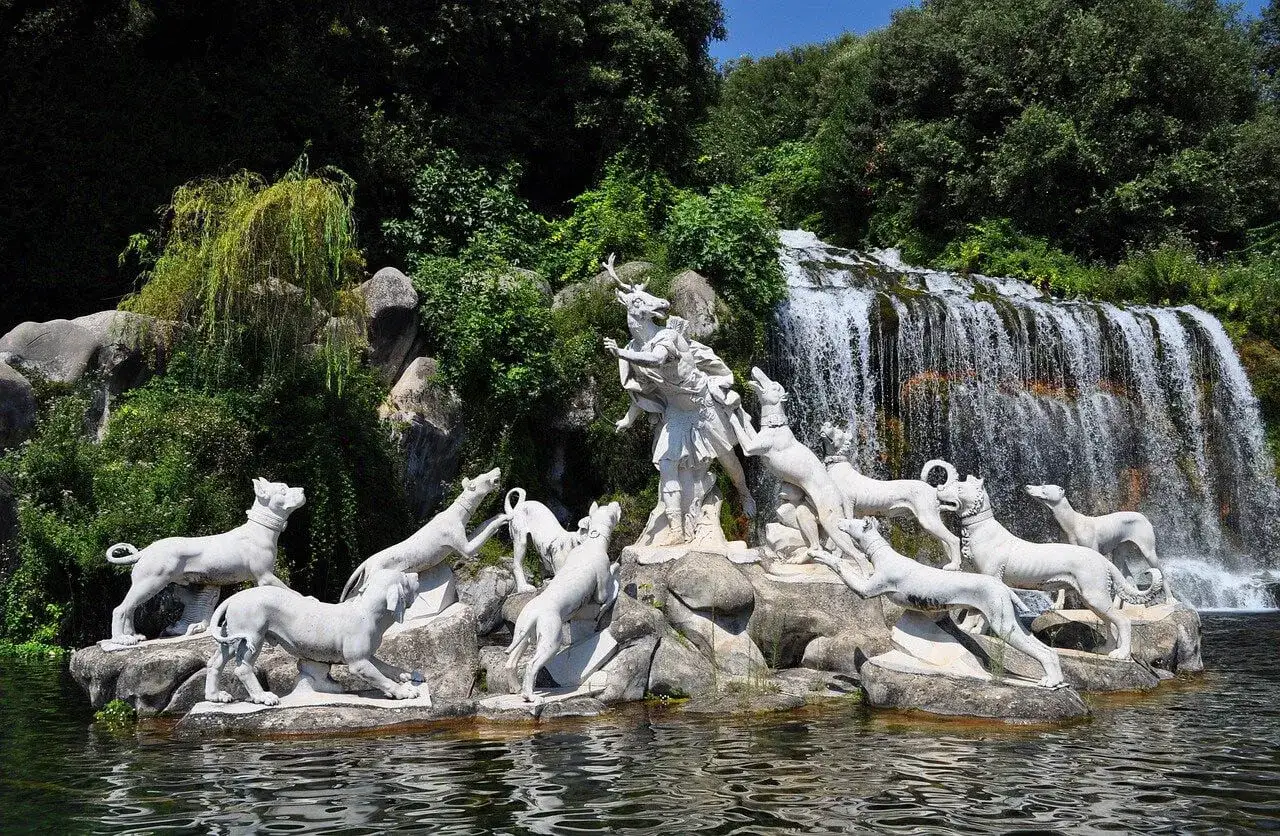Statua di un uomo con cervo e cani, parte del giardino del **regno delle due Sicilie**, con cascata sullo sfondo.