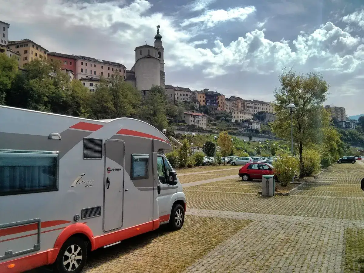 Camper in sosta a Belluno, con case colorate e campanile sullo sfondo.
