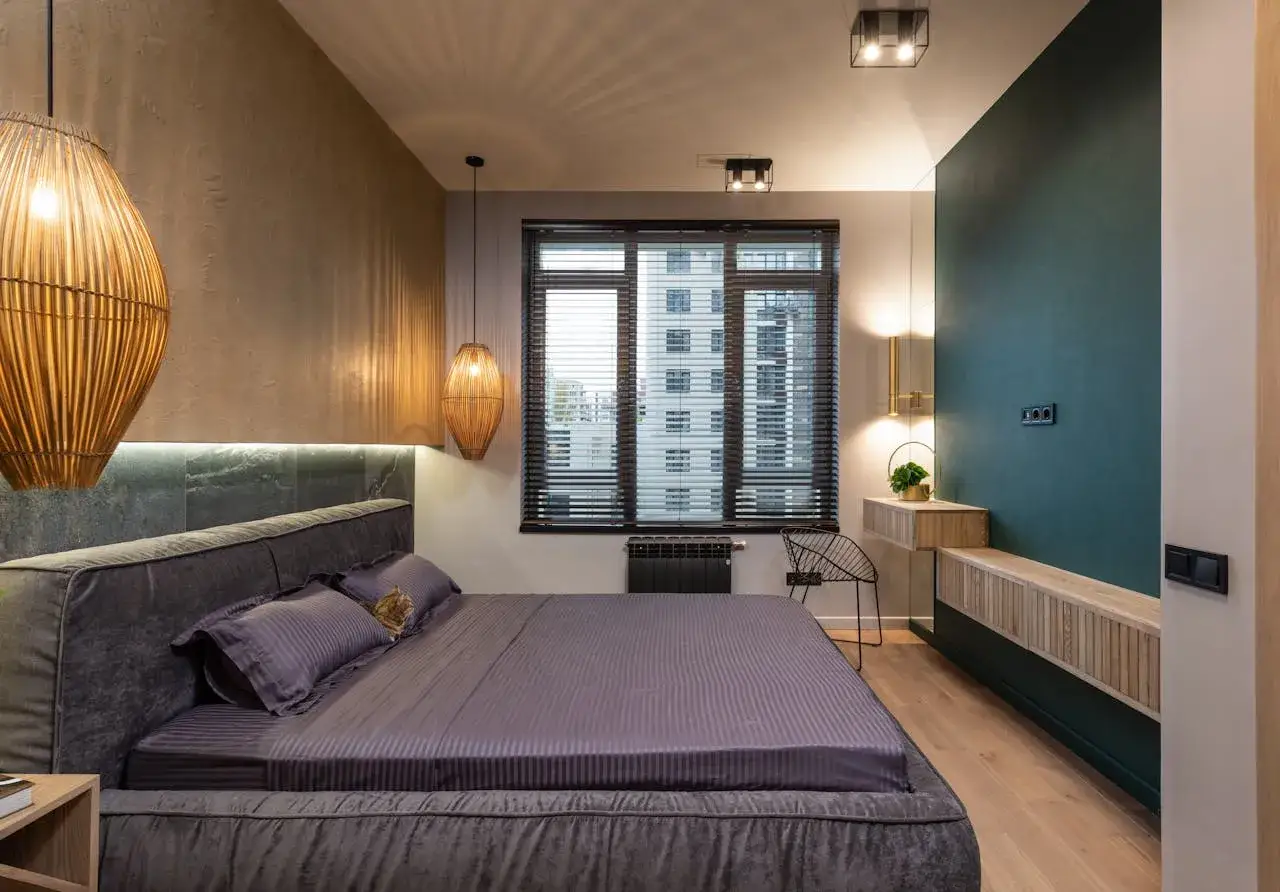 Elegante habitaci&oacute;n con cama gris, l&aacute;mparas de mimbre y pared verde. Los colores de la habitaci&oacute;n crean un ambiente acogedor y moderno.
