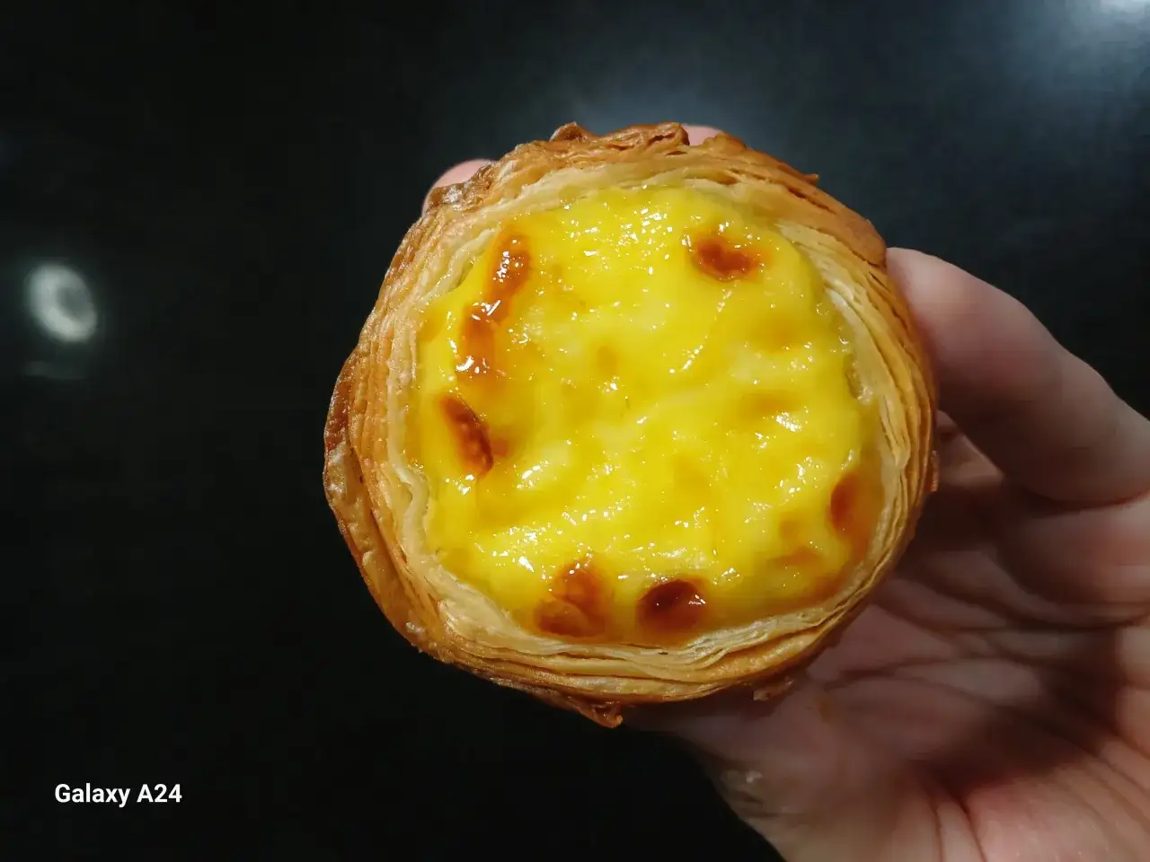 En hand håller en gyllene, krispig pastel de nata med krämig vaniljkräm och karamelliserade toppar.