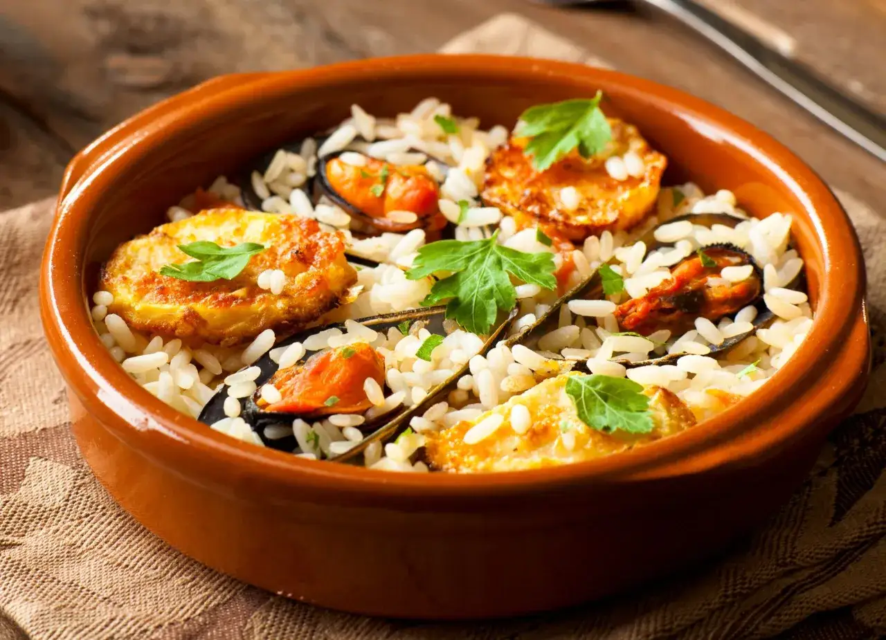 Un saporito piatto di riso patate e cozze, guarnito con prezzemolo fresco, servito in una ciotola di terracotta.