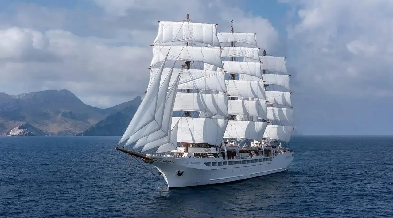 Ein majest&auml;tisches Segelschiff mit vollen wei&szlig;en Segeln, das auf dem blauen Meer f&auml;hrt. Dieses Schiff k&ouml;nnte leicht zu den 10 besten Kreuzfahrtschiffen z&auml;hlen.