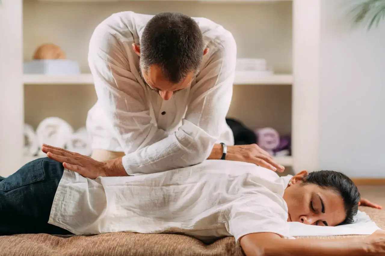Mężczyzna wykonuje masaż shiatsu na leżącej kobiecie. Terapeuta naciska plecy pacjentki, która odpoczywa.