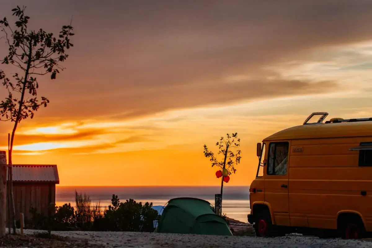 Un camping-car jaune et une tente verte campent face à un coucher de soleil spectaculaire sur la côte. Un rêve d'évasion à Arcachon.