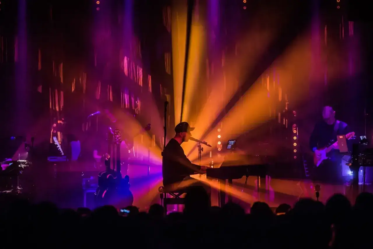 Muzyk gra na keyboardzie podczas jednego z niezapomnianych **koncertów**. W tle gitary i światła tworzą magiczną atmosferę.