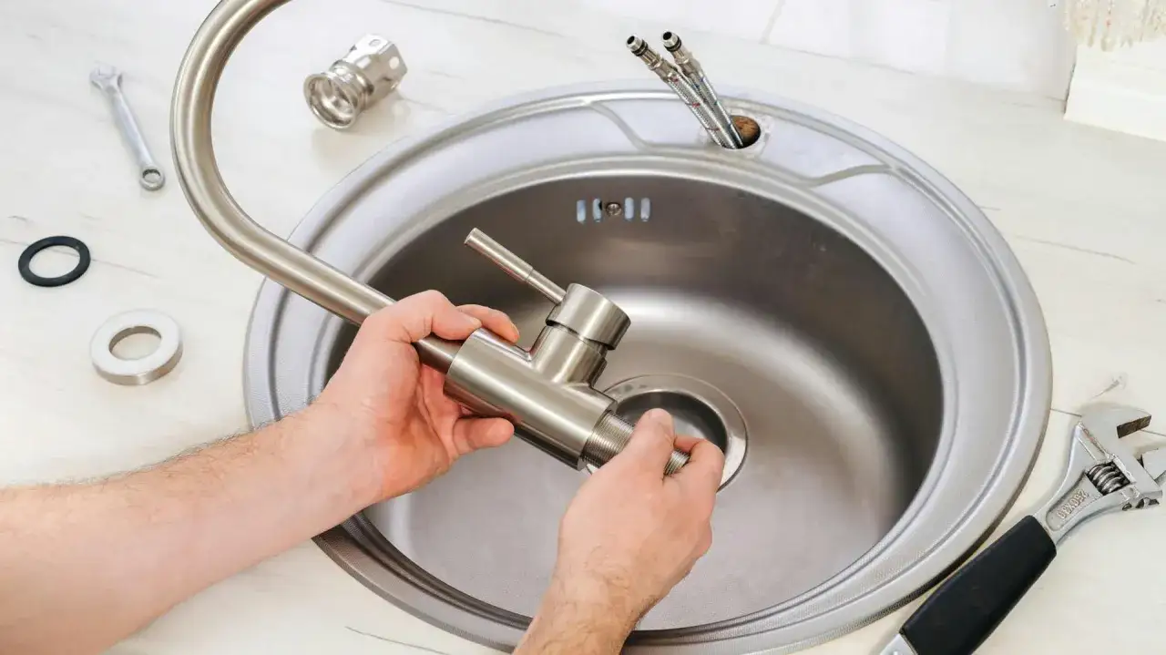 Wymiana baterii kuchennej w toku. Dłonie montują nową baterię w zlewie, obok klucz i uszczelki.