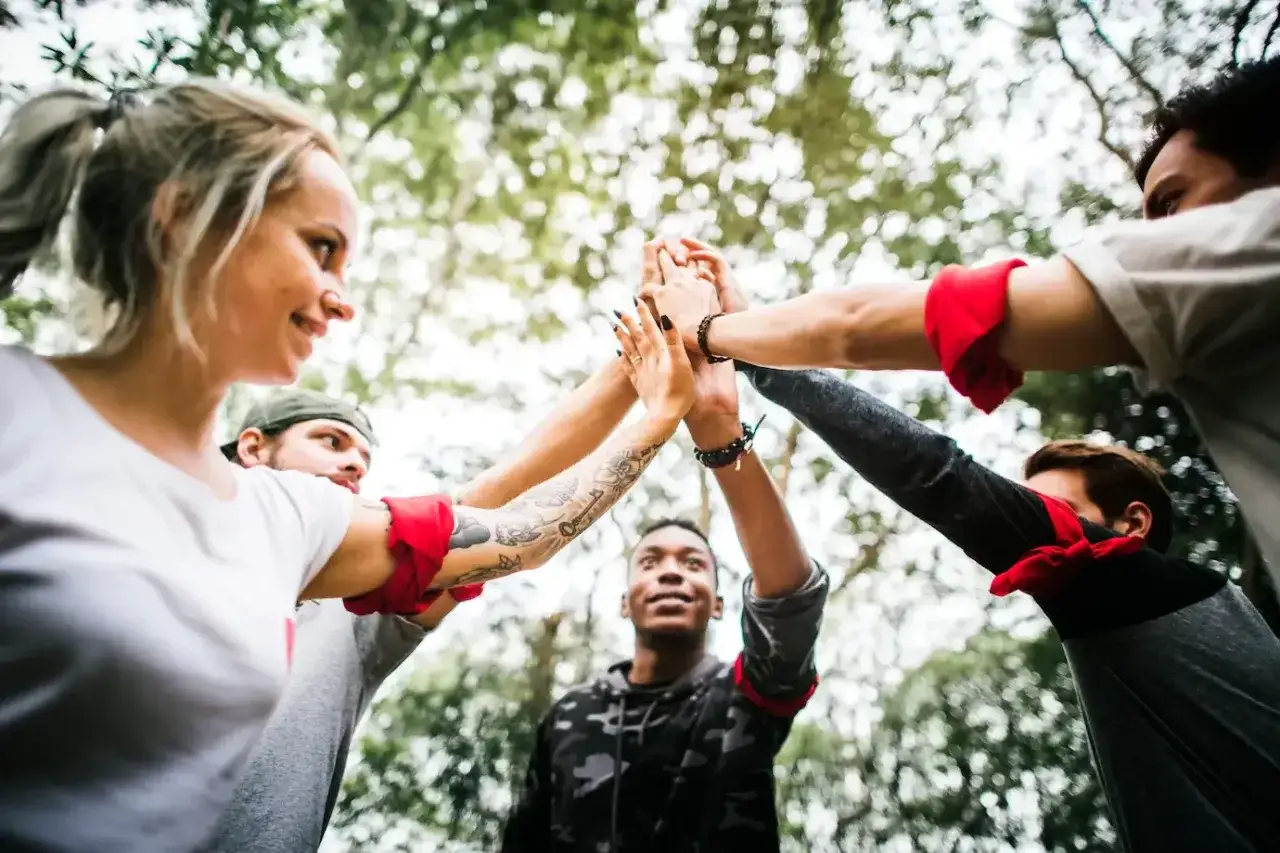 En grupp kollegor ger varandra high-fives utomhus, en perfekt id&eacute; f&ouml;r tips p&aring; aktiviteter med kollegor som st&auml;rker teamk&auml;nslan.