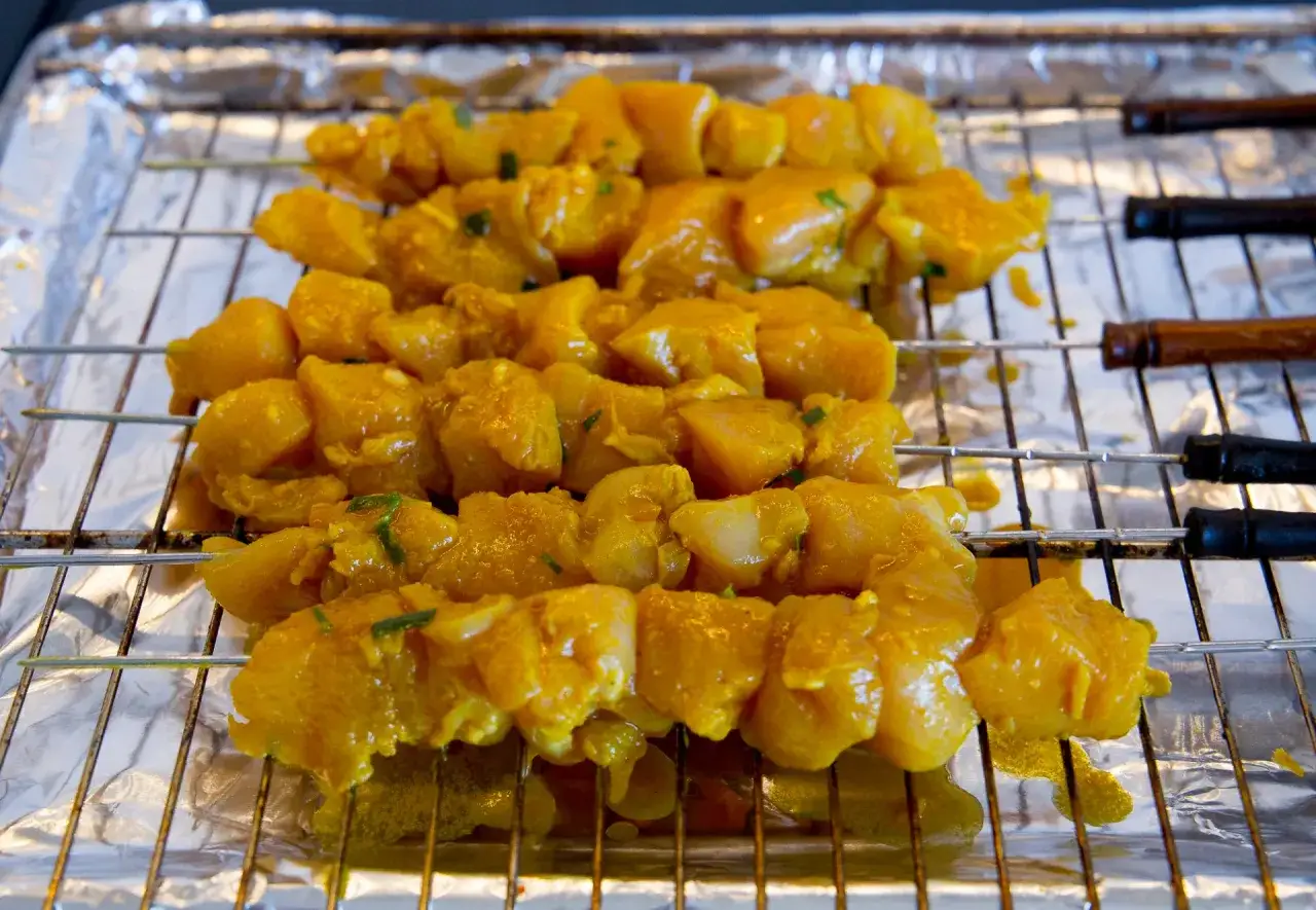 Rå kyckling satay på spett, marinerad i en gul kryddblandning, redo att grillas.