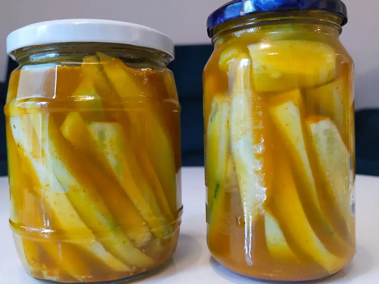 Dwa słoiki z ogórkami w zalewie curry. Kawałki ogórków zanurzone w złocistej, aromatycznej zalewie.