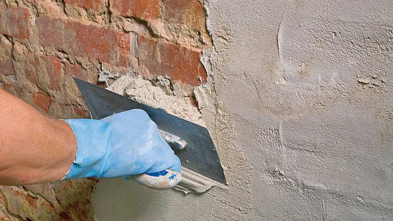 Hand mit blauer Handschuh tr&auml;gt mit Kelle **Sanierputz** auf feuchte Ziegelwand im **Keller** auf.