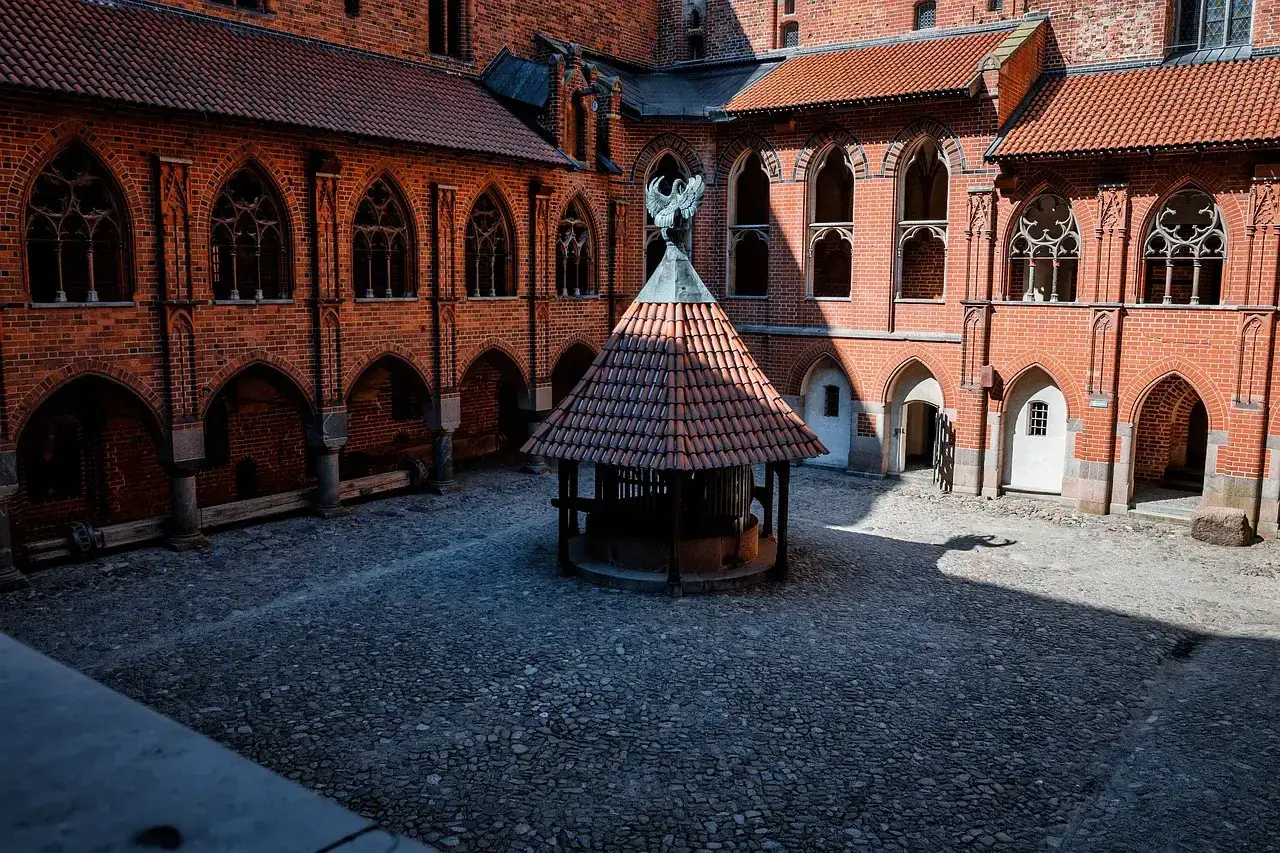 Dziedziniec zamku w Malborku, z kamienną studnią i ceglanymi arkadami. Warto zobaczyć, świetne zamek w Malborku opinie!