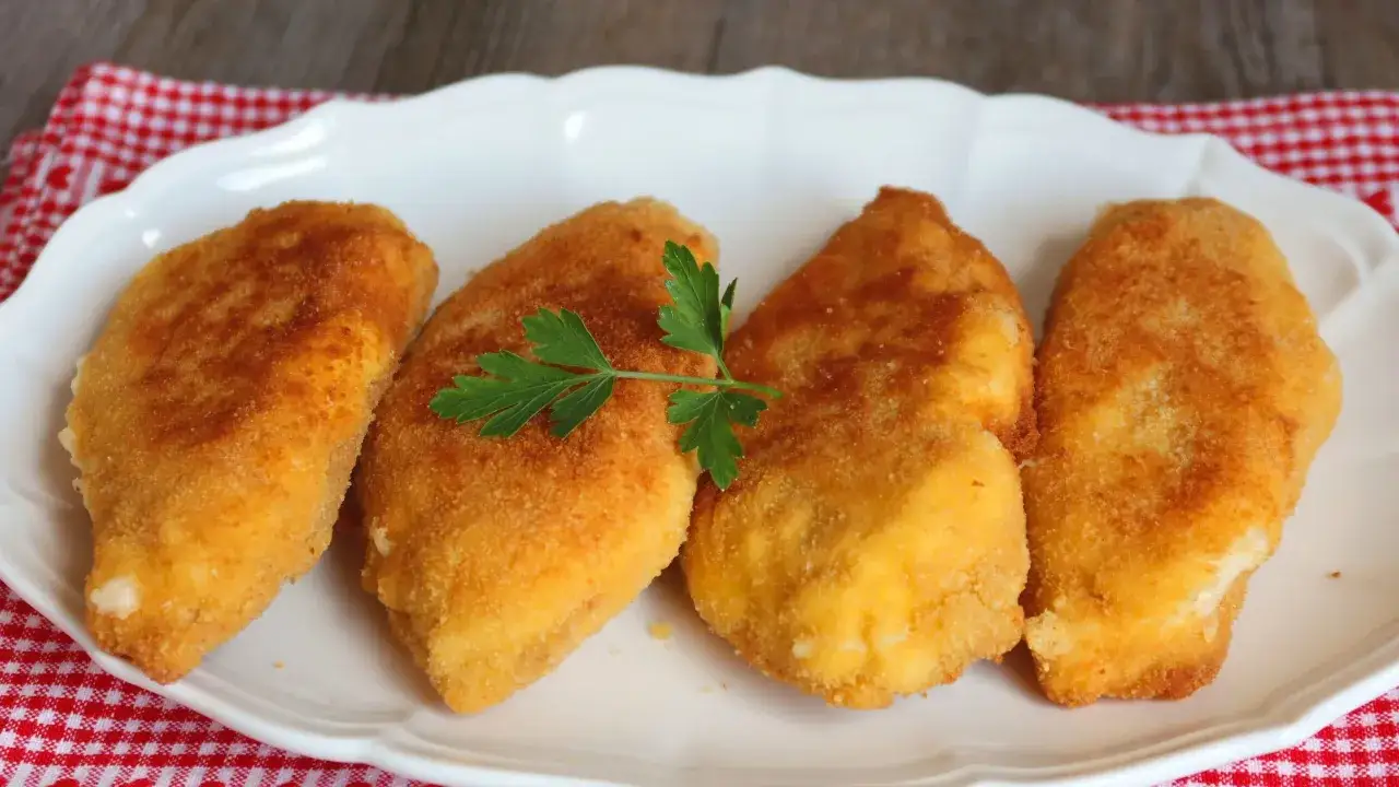 Cuatro pechugas villaroy doradas y crujientes, servidas en un plato blanco con una ramita de perejil.