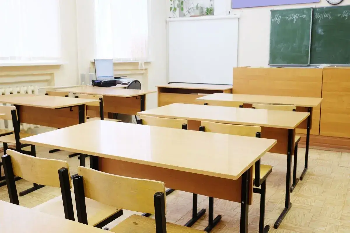 Puste ławki i krzesła w sali lekcyjnej, gotowe na lekcję. Widać tablicę, projektor i komputer. Takie przedmioty są w siódmej klasie.