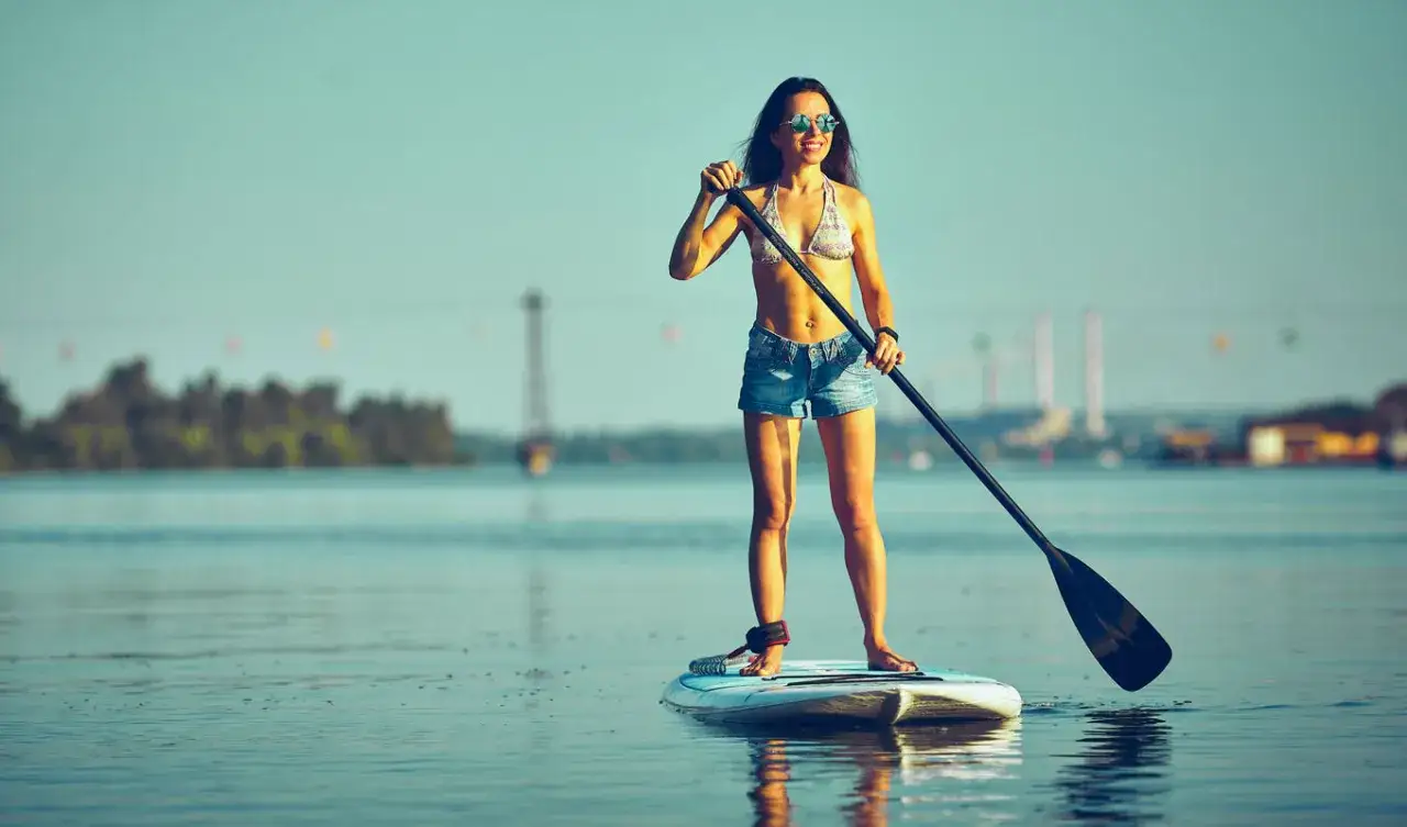 Frau auf Stand Up Paddle Board, achtet auf Balance. Sonnige Tage auf dem Wasser genießen.