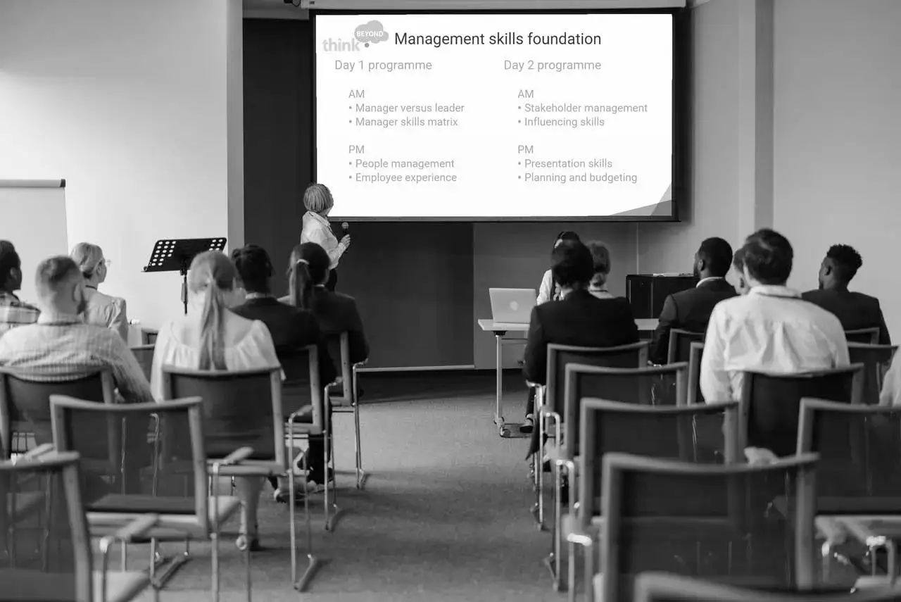 A trainer leads a corporate executive training session on management skills, with attendees seated in a conference room.