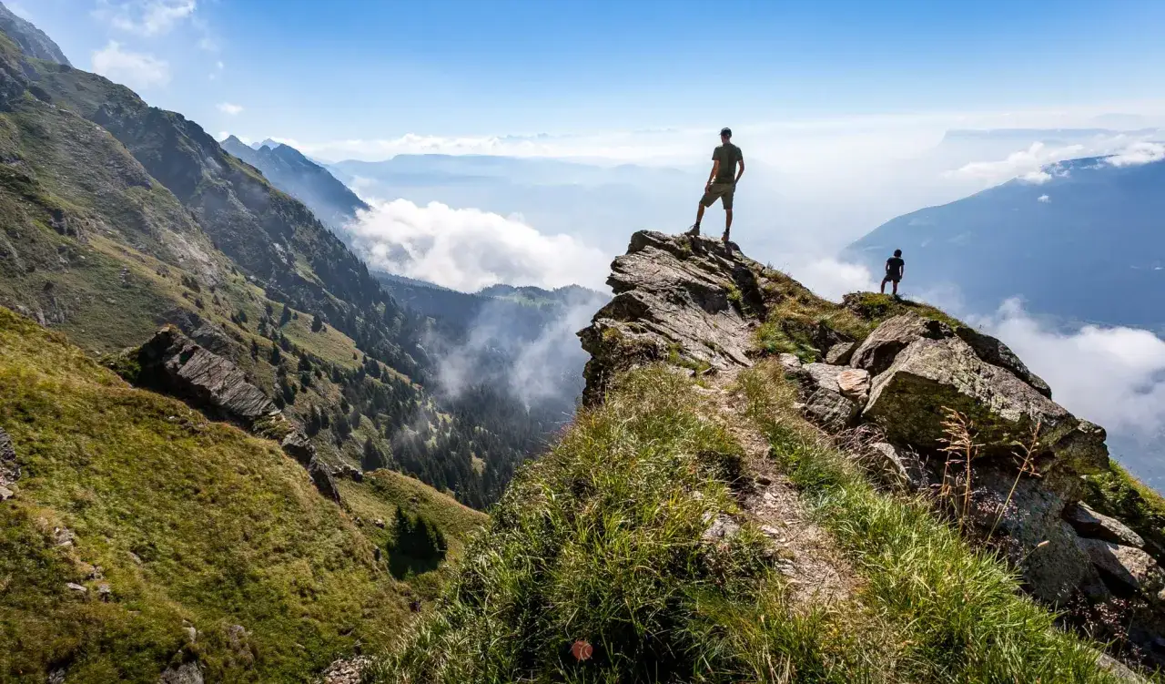 Zwei Wanderer stehen auf einem Felsvorsprung und blicken &uuml;ber nebelverhangene T&auml;ler und Berge. Die Spronser Seen sind in der Ferne zu erahnen.