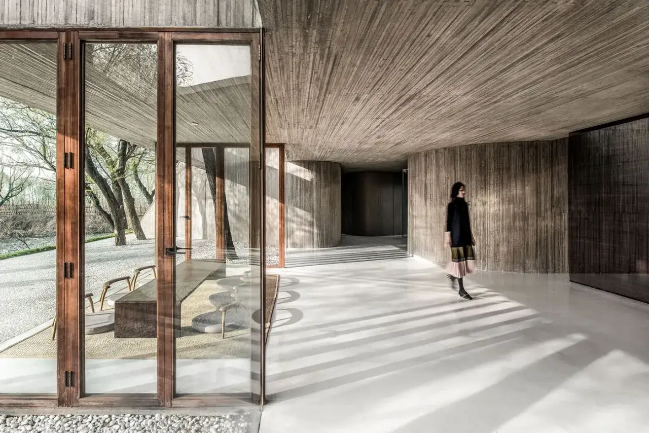 Interno moderno con pareti e soffitto in cemento grezzo. Un pavimento bianco lucido riflette le ombre delle persiane.