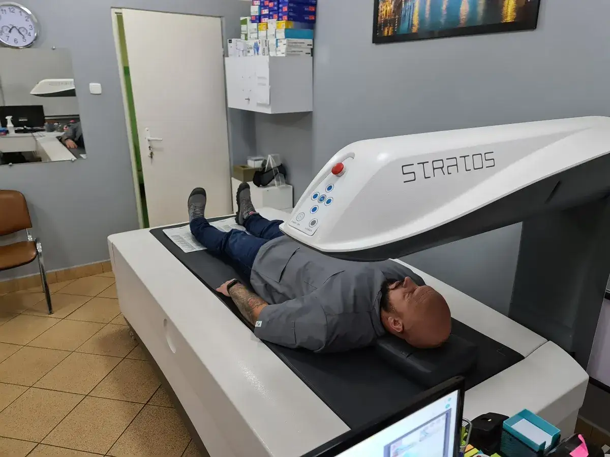 Mężczyzna leży na łóżku aparatu Stratos, który wykonuje badanie densytometryczne.