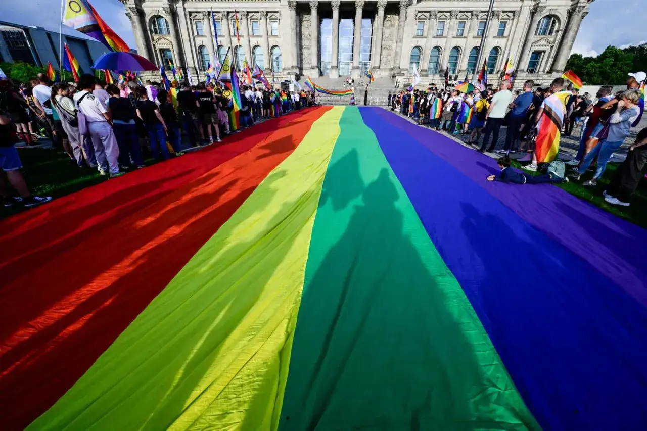 A massive rainbow flag unfurls before the Reichstag building, a vibrant symbol of pride and inclusivity, suggesting Germany is gay friendly.