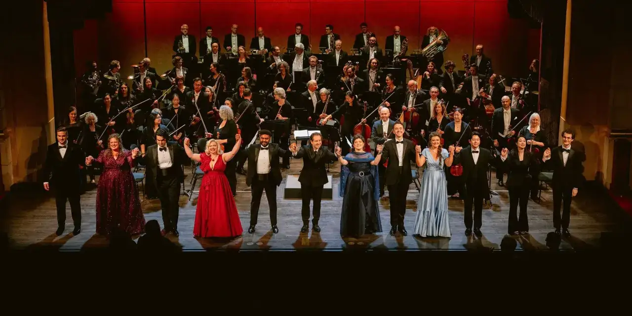 Artyści na scenie, w tym soliści i orkiestra, dziękują publiczności. To piękny obraz tego, czym jest opera.